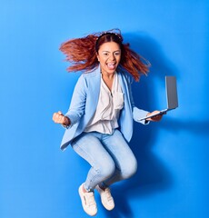 Young beautiful latin businesswoman smiling happy celebrating success. Jumping with smile on face using laptop over isolated blue background