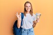 © Krakenimages.com - Beautiful blonde woman wearing student backpack and holding canadian dollars doing ok sign with fingers, smiling friendly gesturing excellent symbol