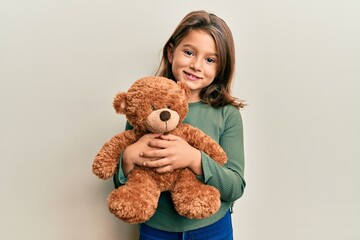 little beautiful girl hugging teddy bear smiling with a happy and cool smile on face. showing teeth.