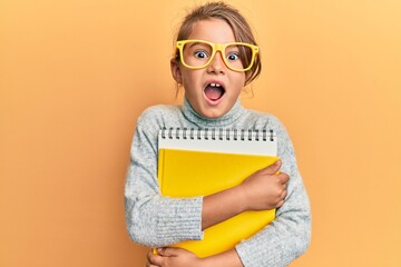 Wall Mural - Little beautiful girl wearing glasses and holding books celebrating crazy and amazed for success with open eyes screaming excited.