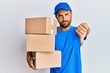 © Krakenimages.com - Handsome man with beard wearing courier uniform holding delivery packages looking unhappy and angry showing rejection and negative with thumbs down gesture. bad expression.