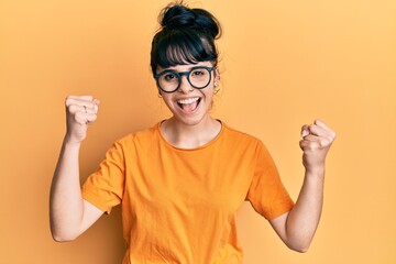 Young hispanic girl wearing casual clothes and glasses screaming proud, celebrating victory and success very excited with raised arms