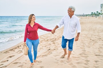 Middle age hispanic couple smiling happy walking at the beach.