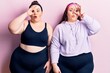 Young plus size twins wearing sportswear doing ok gesture shocked with surprised face, eye looking through fingers. unbelieving expression.