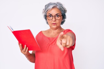 Wall Mural - Senior hispanic woman wearing glasses holding book pointing with finger to the camera and to you, confident gesture looking serious