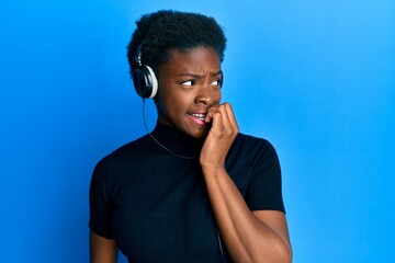 Poster - Young african american girl listening to music using headphones looking stressed and nervous with hands on mouth biting nails. anxiety problem.