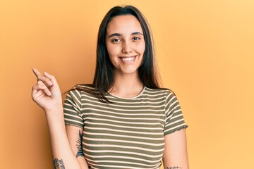 Young hispanic woman wearing casual striped t shirt smiling happy pointing with hand and finger to the side