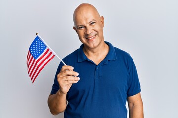 Wall Mural - Middle age bald man holding united states flag looking positive and happy standing and smiling with a confident smile showing teeth