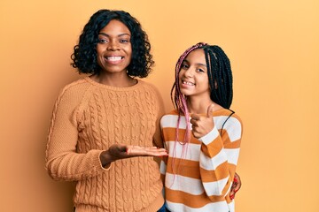 Poster - Beautiful african american mother and daughter wearing wool winter sweater showing palm hand and doing ok gesture with thumbs up, smiling happy and cheerful