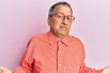 Canvas Print - Middle age indian man wearing casual clothes and glasses clueless and confused expression with arms and hands raised. doubt concept.