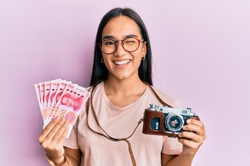 Sticker - Young asian woman holding vintage camera and 100 chinese yuan winking looking at the camera with sexy expression, cheerful and happy face.