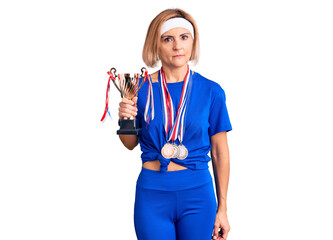 Canvas Print - Young blonde woman holding champion trophy wearing medals thinking attitude and sober expression looking self confident