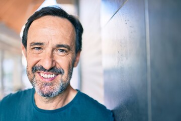 Middle age man with beard smiling happy outdoors leaning on the wall