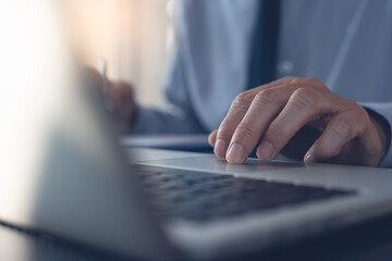 Wall Mural - Businessman working on laptop computer surfing the internet on office table, close up