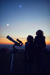 mother and daughter observing stars, planets, moon and night sky with astronomical telescope.