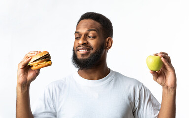 Wall Mural - African Man Choosing Between Burger And Apple Standing In Studio