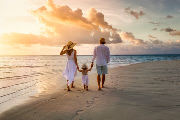a elegant family in white summer clothing walks hand in hand down a tropical paradise beach during s
