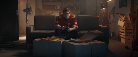 Wall Mural - POV Portrait of Caucasian teenager playing video game inside home garage, enjoying pizza. Shot with 2x anamorphic lens