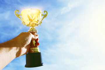 Wall Mural - man holding up a trophy cup as a winner against the blue sky. award and victory concept