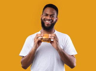 Wall Mural - Cheerful African Man Posing With Burger Standing In Studio