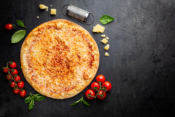 Poster - Tasty cheese pizza and cooking ingredients tomatoes and basil on black background. Top view