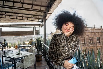 Happy afro young woman with their eyes closed and smiling after receiving some good news. Standing on a beautiful terrace with cactus in the background.