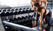 © NVB Stocker - Personal fitness trainer assisting attractive woman with workout at gym health club. Young Woman lifting dumbbell with male trainer. Fitness Healthy lifestye and workout at gym concept.