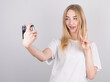 © Studio Nova - Photo of blonde girl in casual t-shirt showing peace sign and taking selfie with old camera