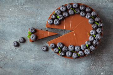 Wall Mural - Chocolate brown cheesecake cut with fresh blueberries on vintage concrete background. Flat lay