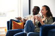 © Southworks - Smiling Young Couple Relaxing At Home Sitting On Sofa Watching On Demand TV Together