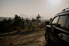 Interesting Travel Adventure Tourism In The Mountains. Sunny Sunset. The Car Stands And Looks Towards The High Hills.