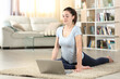 © PheelingsMedia - Woman doing yoga watching video tutorial on laptop