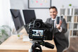 © LIGHTFIELD STUDIOS - selective focus of digital camera near businessman holding smartphone with blank screen during video streaming on blurred background