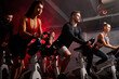 men and women biking in gym, exercising legs doing cardio workout cycling bikes, spinning in health club, wearing tracksuit sportive outfit