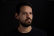 © Alejandro - Young man head shot with black background. He is serious. He has a casual look with beard and t-shirt.