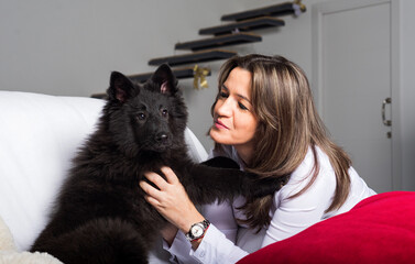 A woman on the sofa looks lovingly at her dog, a Belgian shepherd's puppy groenendael.