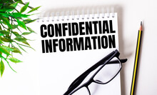 CONFIDENTIAL INFORMATION Is Written In A White Notebook Next To A Pencil, Black-framed Glasses And A Green Plant.