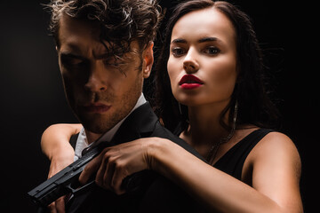 dangerous woman holding gun and hugging man in suit isolated on black