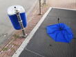 Blauer Mülleimer und blauer Regenschirm bei windigem Wetter auf dem Lüftungsschacht der U-Bahn Station an der Senckenberganlage im Westend von Frankfurt am Main in Hessen