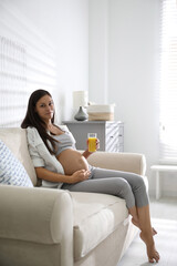 Poster - Young pregnant woman with glass of juice in living room. Taking care of baby health