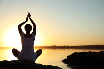 Wall Mural - Woman practicing yoga near river on sunset. Healing concept