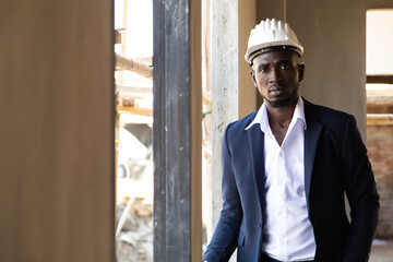 african american businessman  in protective safety hard hat looking at blueprint plans on construction site.