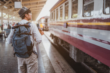 Asian man traveler with backpack in the railway, Backpack  and wearing hat at the train station with a traveler. Travel concept. Man traveler tourist walking at train station.