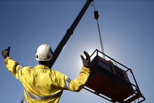 Rigger Wearing A Glove Standing Raising Using His Hands Signal By Moving Finger Slowly To Directing Communication With Crane Driver To Move The Boom Up At Construction Site, Sydney, Australia   