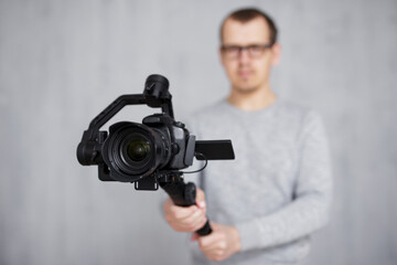 Wall Mural - close up of modern dslr camera on 3-axis gimbal stabilizer in videographer hands over grey