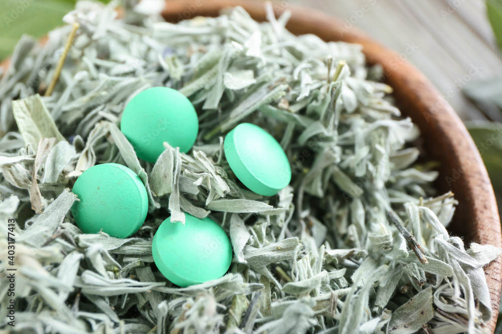 Plant based pills in bowl with dry herbs