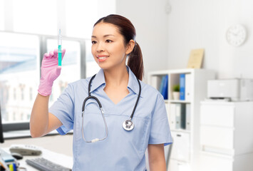 Wall Mural - medicine, vaccination and healthcare concept - happy smiling asian female doctor or nurse in blue uniform with stethoscope and syringe over hospital background