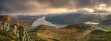 Panorama Of Dramatic Clouds With A View Over Ullswater In The Lake District As Shafts Of Sunlight Casts Rays Over Glenridding Village