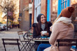 © Monkey Business - Two Female Friends Meeting Sitting Outside Coffee Shop On City High Street