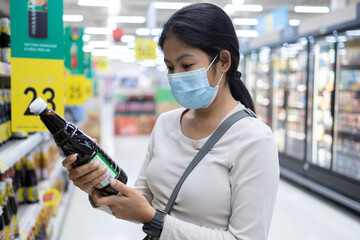 Asian woman wearing face mask shopping in supermarket, Women pick up food on shelves during coronavirus or COVID-19 outbreak.